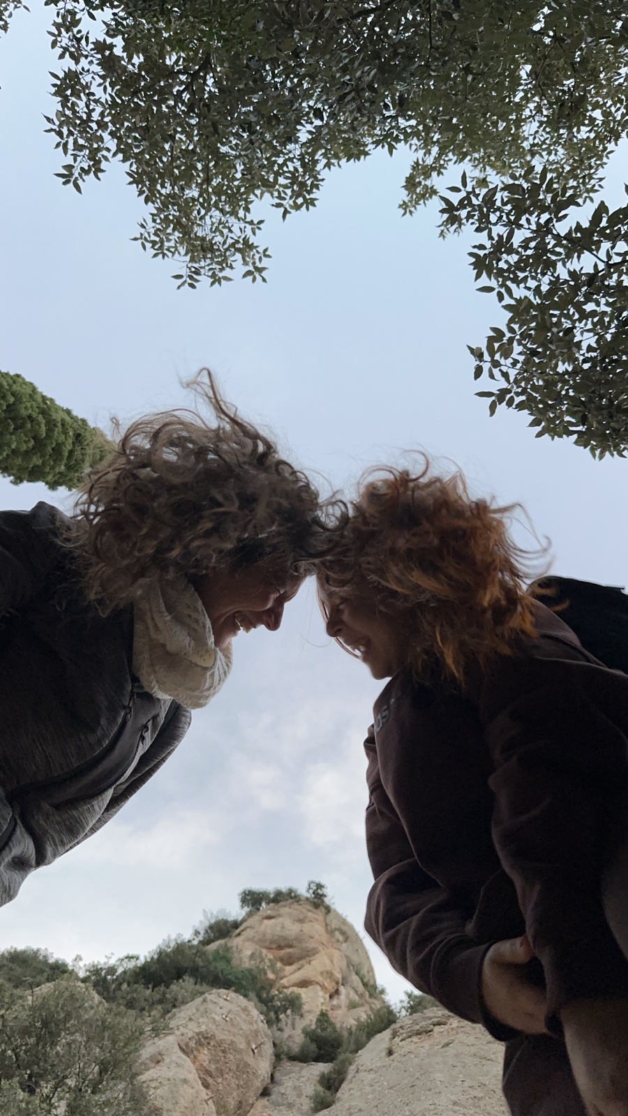 Ariela i Ari somrient juntes sota el cel, entre arbres i muntanyes